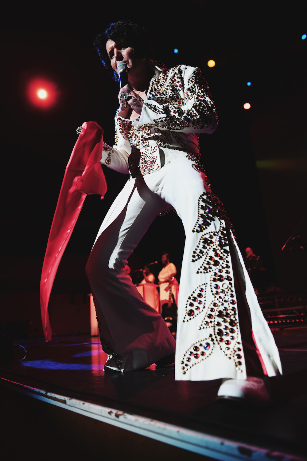 Rob Kingsley performing A Vision of Elvis live on stage in the Stone & Flame Elvis jumpsuit under red concert lights